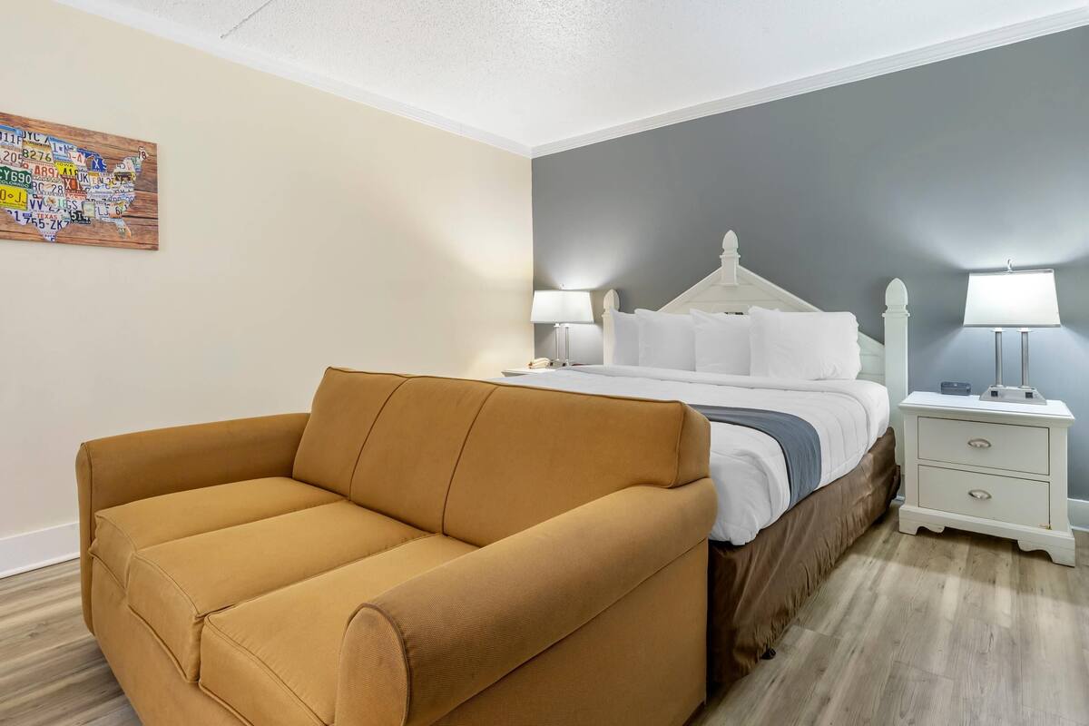 Habitación de hotel con cama, mesita de noche, lámpara, sofá y un mapa en la pared.