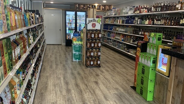 A liquor store with wooden flooring, shelves stocked with various bottles, and a refrigerated display case in the background. - Econo Lodge Conway Central (Conway)