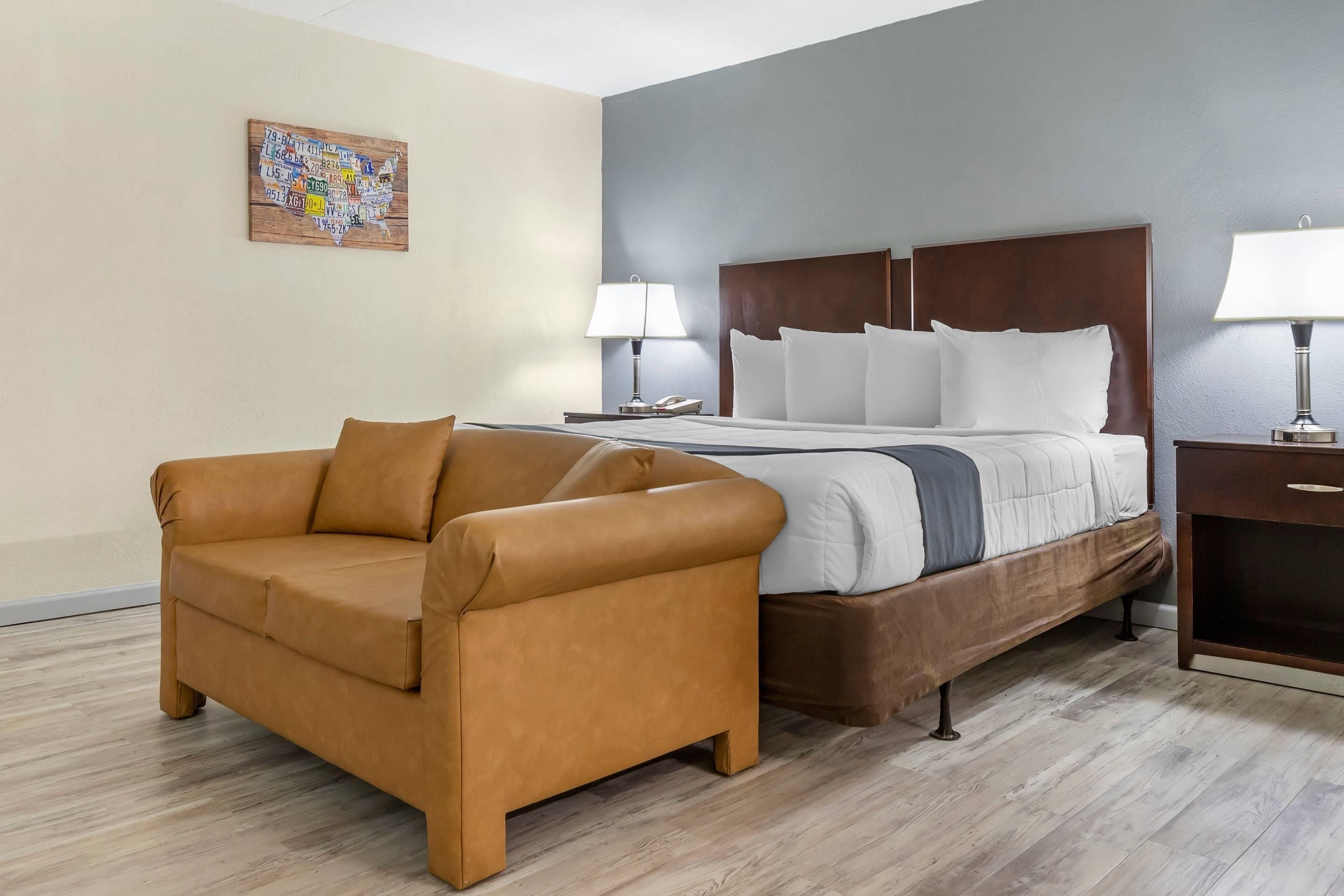 A hotel room with a bed, a sofa, a nightstand, and a wall-mounted lamp.