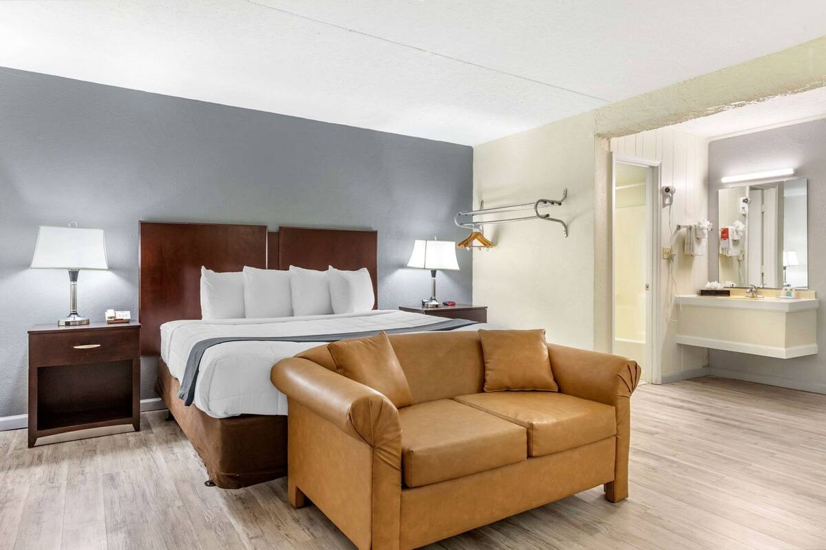 Una habitación de hotel con cama, mesitas de noche, un sofá y un baño con lavabo y espejo.