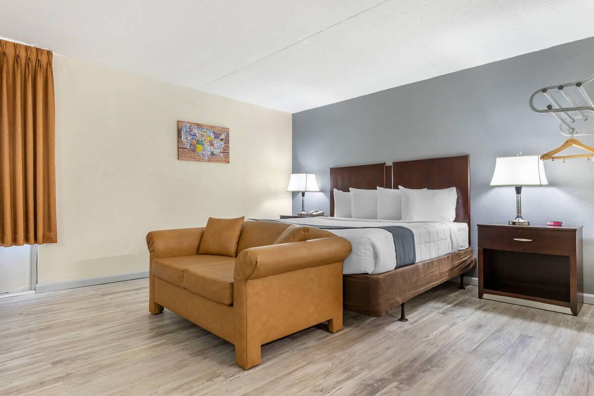 Habitación de hotel con cama, sofá, mesita de noche con lámpara y una lámpara de pared.