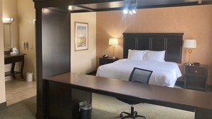 A hotel room with a large bed, a desk, a chair, a nightstand, a lamp, and a framed picture on the wall. - Hampton Inn & Suites Carlsbad (Carlsbad)