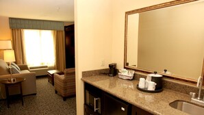 A hotel room with a kitchenette, a sofa, a chair, a large mirror, and a window with curtains. - Hampton Inn & Suites Carlsbad (Carlsbad)