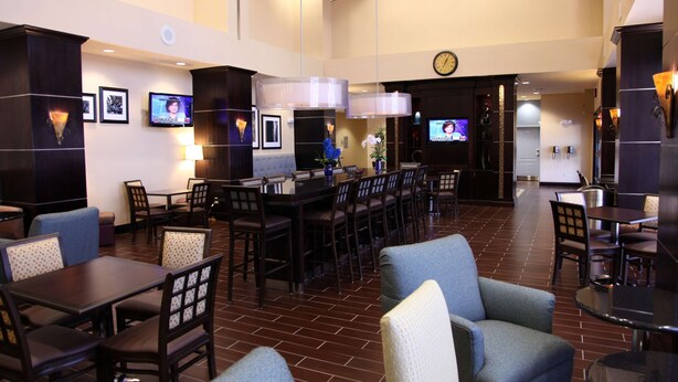 A hotel lobby with multiple dining tables and chairs, a reception desk, and a clock on the wall. - Hampton Inn & Suites Carlsbad (Carlsbad)