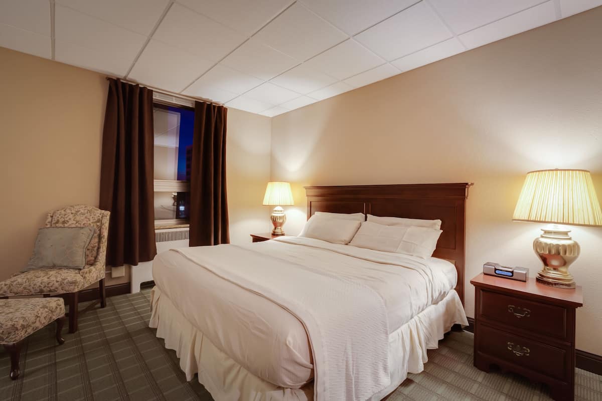 Ein Hotelzimmer mit einem großen Bett, einem Sessel, einem Nachttisch mit Lampe und einem Fenster mit Vorhängen.