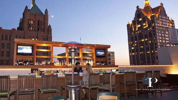 An outdoor bar area with a bar counter, seating, and a view of two buildings.
