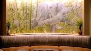 A room with a large mural of an elephant and bamboo, a cushioned seating area, and two vases on a window sill.