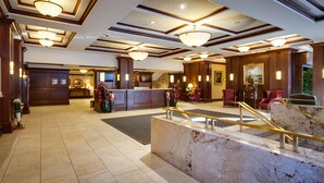 A spacious lobby with a marble reception desk, multiple seating areas, and a high ceiling with decorative lighting.