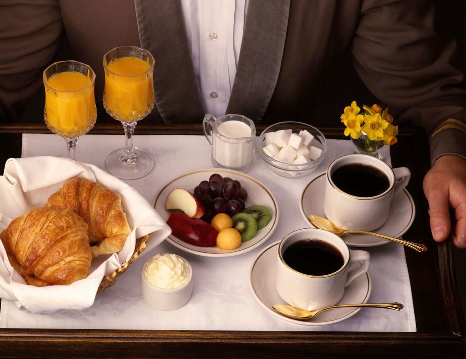 A breakfast tray with croissants, fruit, coffee, and juice glasses.