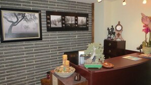 Een receptiebalie met ingelijste foto's aan de muur, een klein beeldje en een bloempot met plant.
