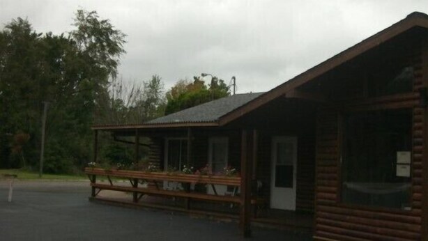 Een vakantiehuisje van hout met een veranda en een bord waarop 'OFFICE' staat.