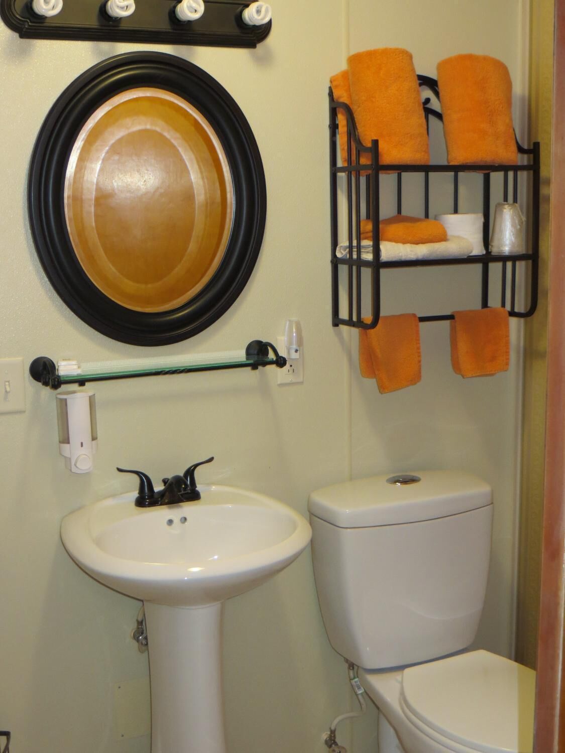 A bathroom with a sink, toilet, and a towel rack with orange towels.