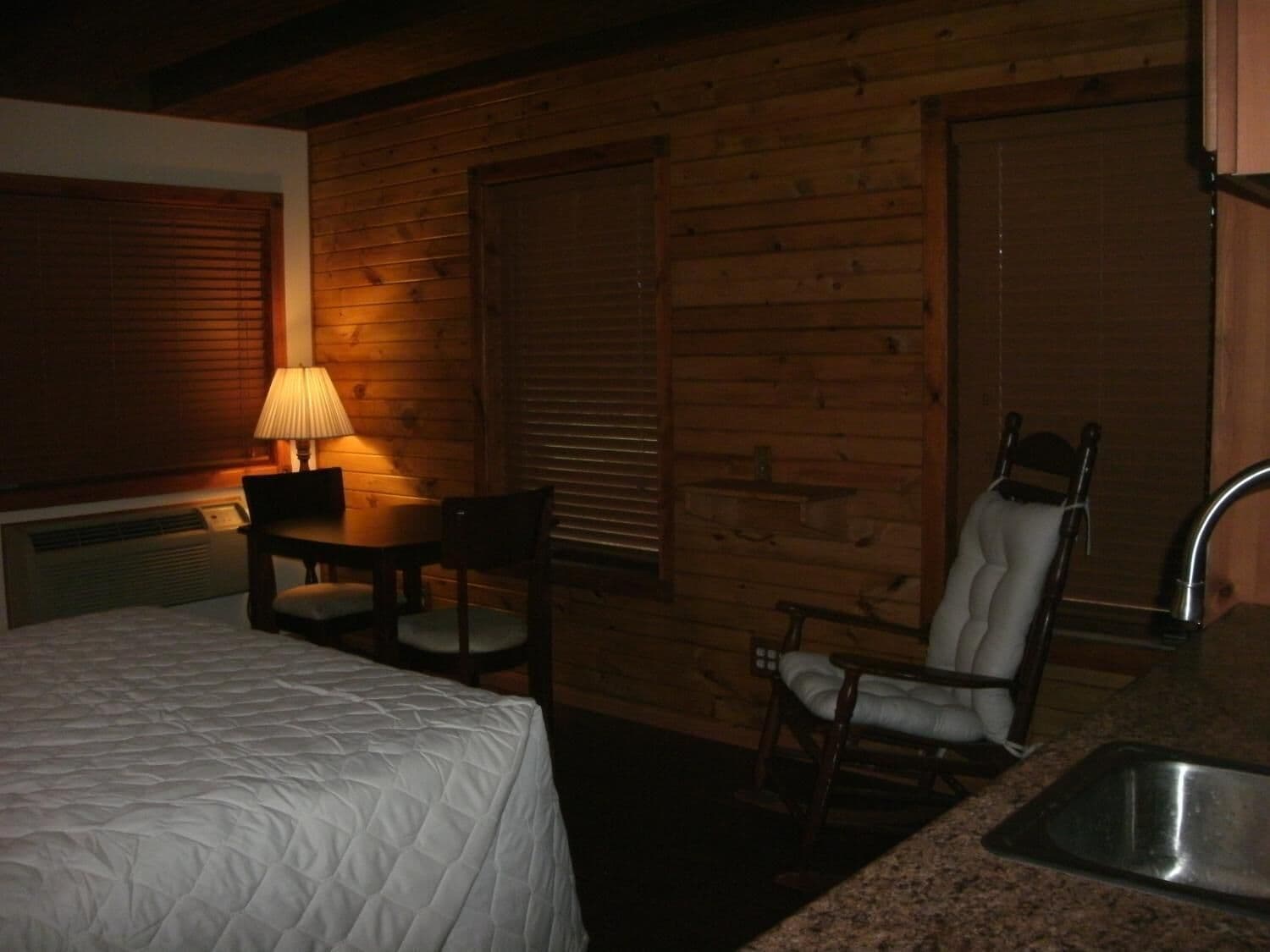 Une pièce confortable avec un lit, une table avec une lampe, une chaise et un lavabo.