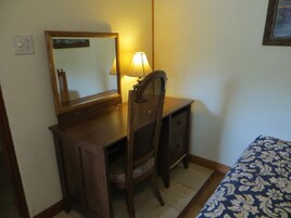 A small, compact room with a wooden desk, a chair, a bedside table, and a bed with a patterned bedspread.