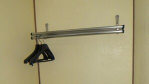 Een kleine kamer met een eenpersoonsbed, nachtkastje en een wandplank met ophanger.