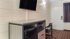 A room with a flat-screen TV mounted on the wall, a microwave in a cabinet, a chair, and a door with a striped curtain.