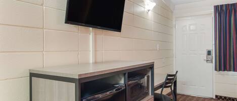 A room with a flat-screen TV mounted on the wall, a microwave in a cabinet, a chair, and a door with a striped curtain.