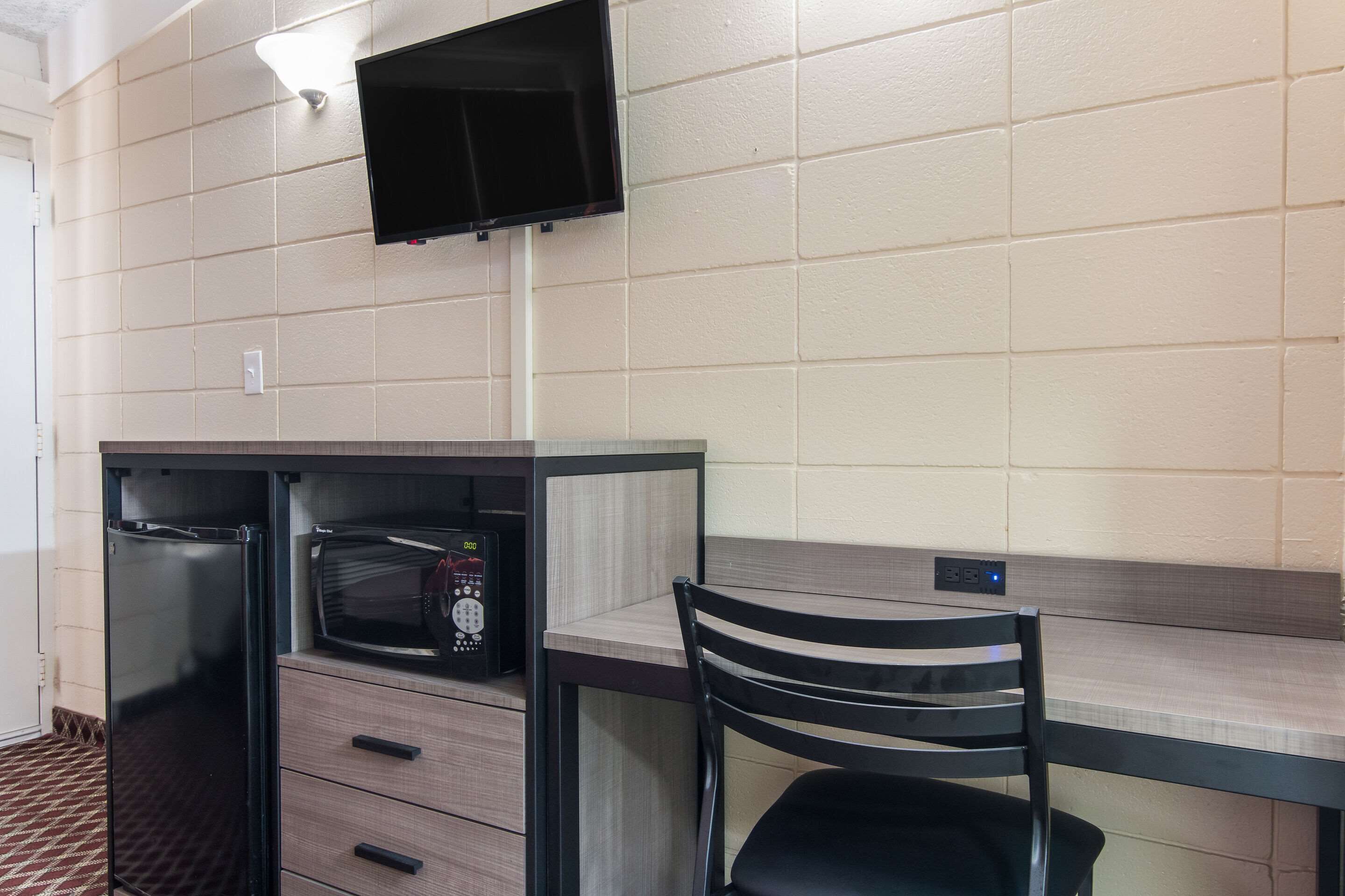 A kitchenette with a microwave, refrigerator, and a small cabinet. There is a chair and a flat-screen TV mounted on the wall.