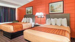 A hotel room with two beds, a nightstand, a lamp, and two paintings on the wall.