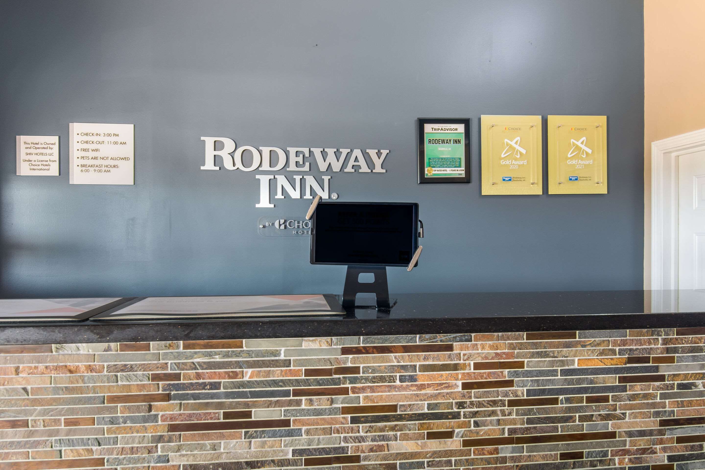 A reception desk with a monitor, a sign for Rodeway Inn, and two TripAdvisor Gold Awards.