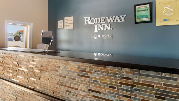A reception desk at Rodeway Inn with a Choice Hotels logo, a TripAdvisor badge, and a Gold Award 2020 plaque.