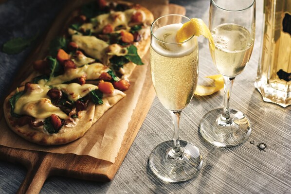 A pizza on a wooden board, two glasses of a clear beverage with lemon, and a bottle in the background.