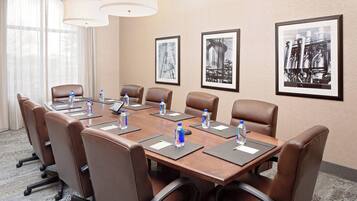 A conference room with a long table, brown leather chairs, water bottles, nameplates, and framed pictures on the wall.