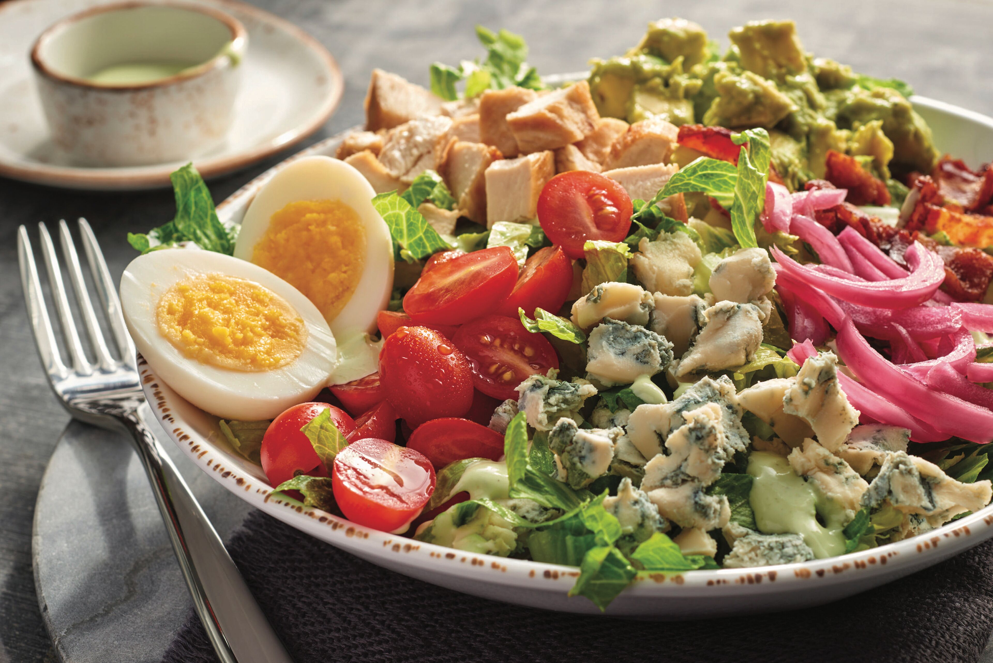 Un piatto di insalata con diversi ingredienti, tra cui pomodori, lattuga e un uovo sodo.