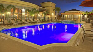 A swimming pool with lounge chairs and umbrellas, surrounded by buildings with outdoor seating areas.