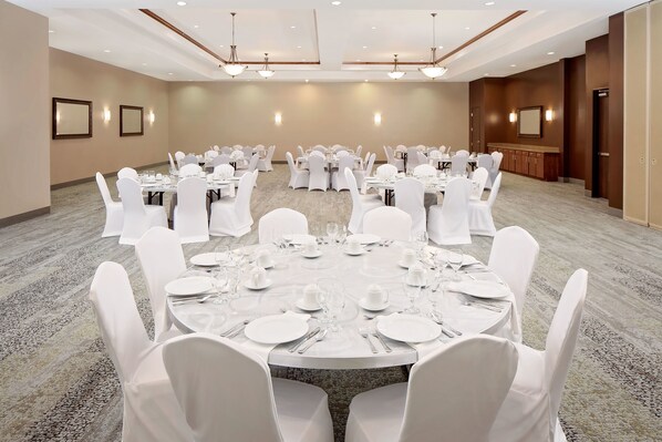A conference room with round tables, white chairs, and a carpeted floor.