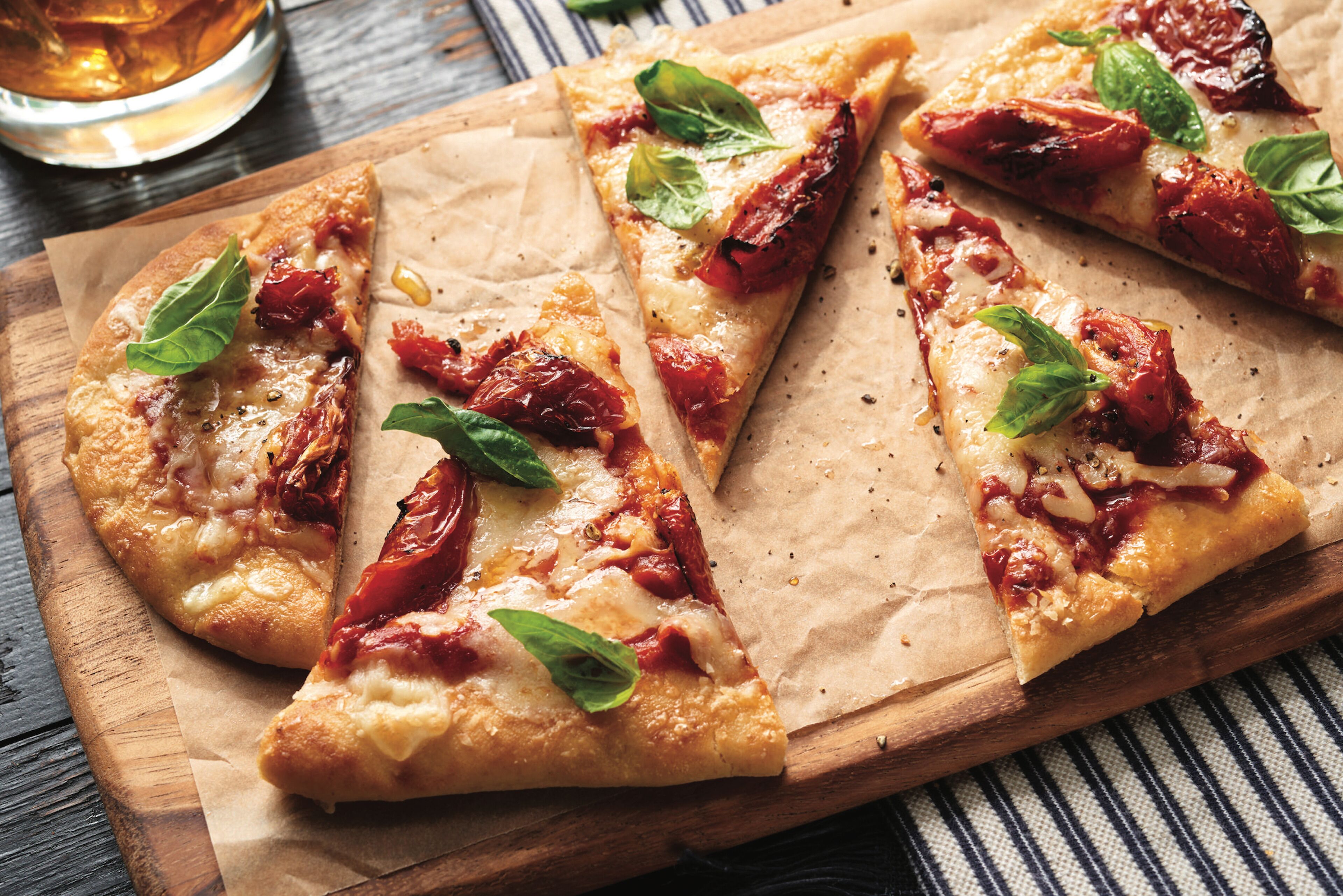Pizza com cobertura de tomate e manjericão sobre uma tábua de madeira.