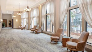 A spacious lobby with a carpeted floor, multiple seating areas, large windows with curtains, and hanging chandeliers.