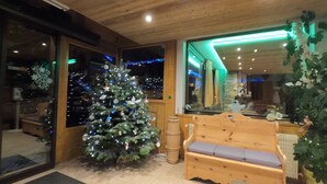 A wooden interior with a Christmas tree, a bench, and a large window. - Le Soly Hotel (Morzine)