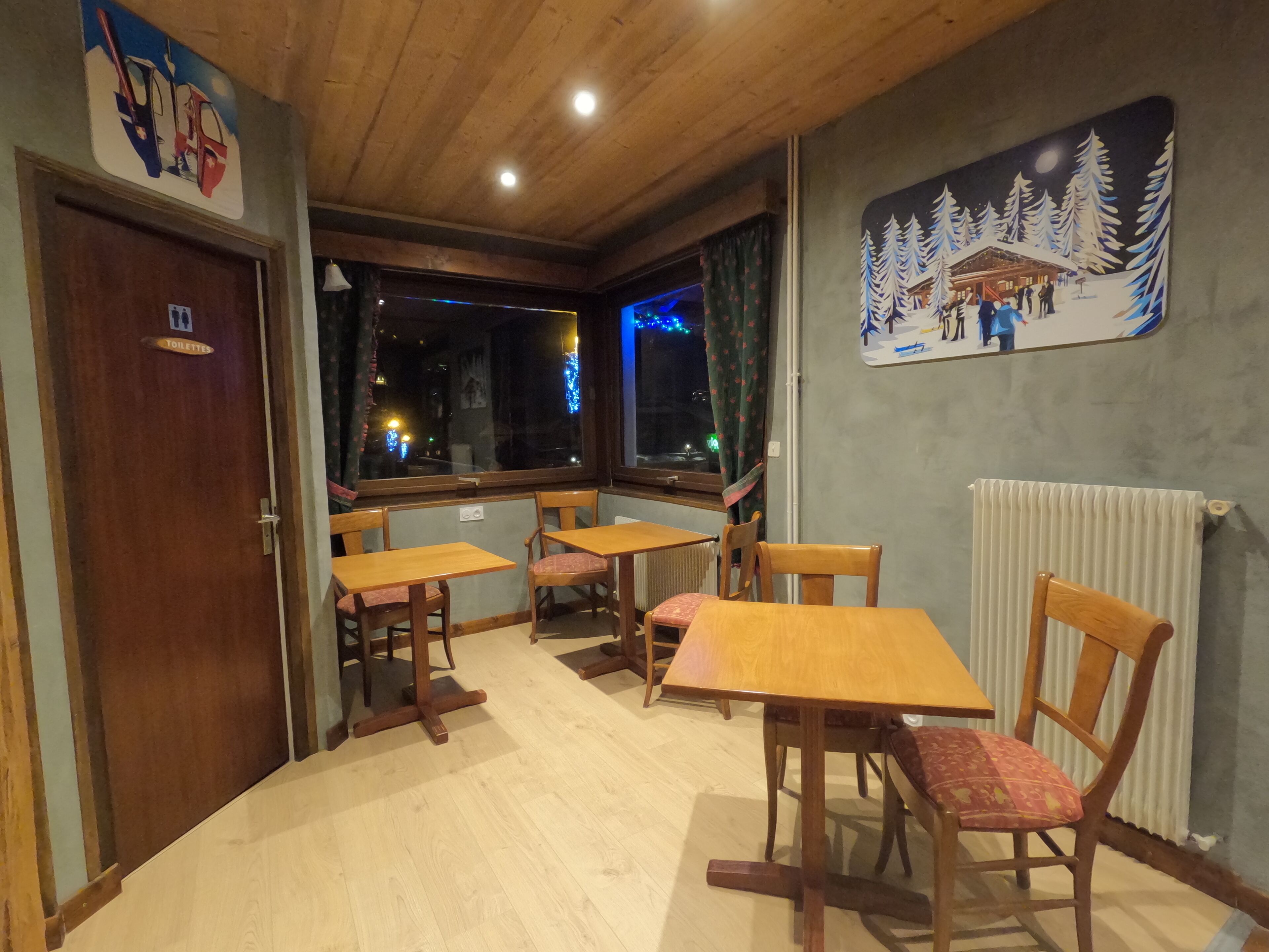 Un comedor acogedor con mesas y sillas de madera, un radiador y un cuadro de un paisaje nevado en la pared.