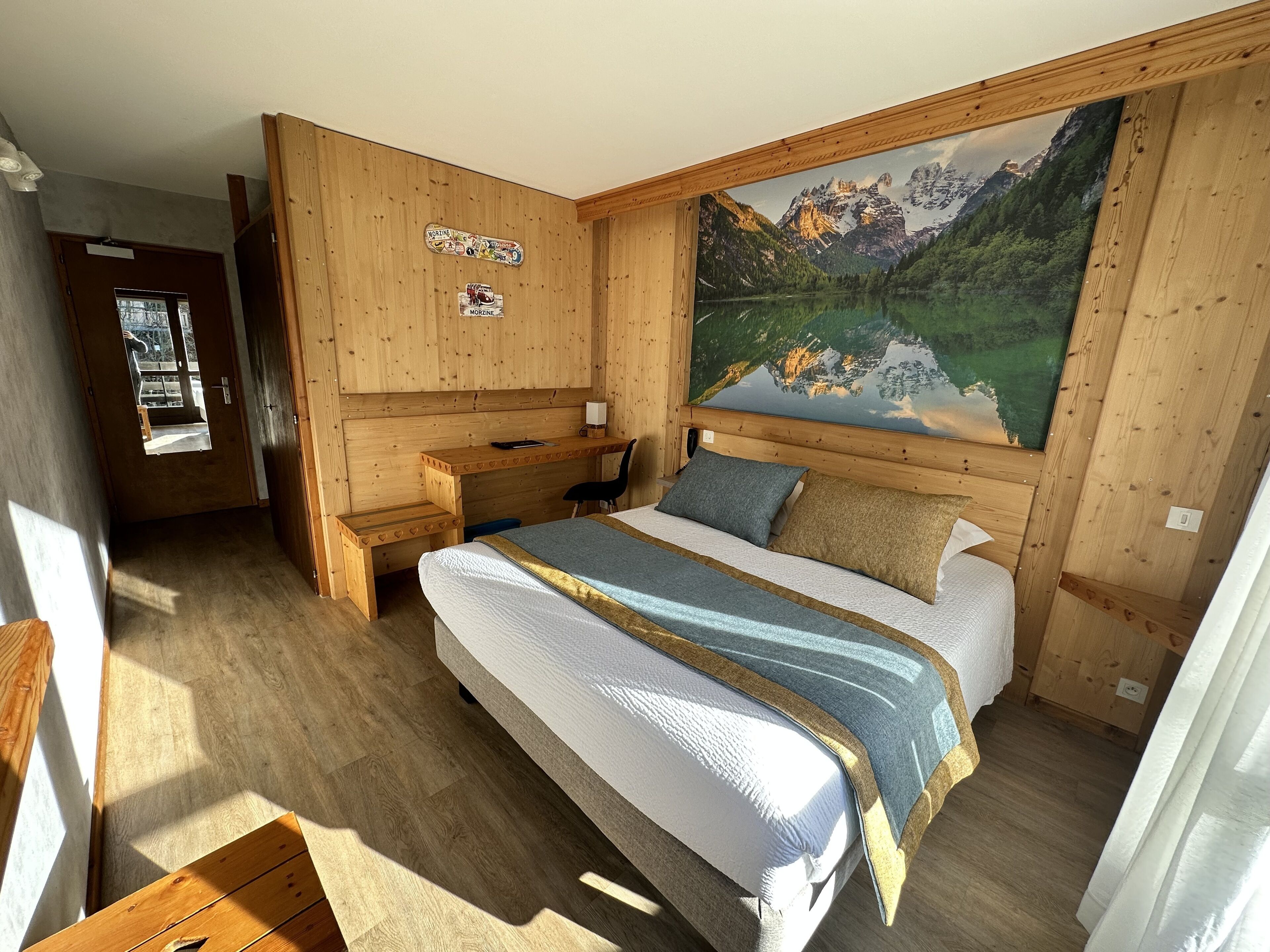 A wooden cabin bedroom with a bed, a desk, and a large painting of a mountain landscape.