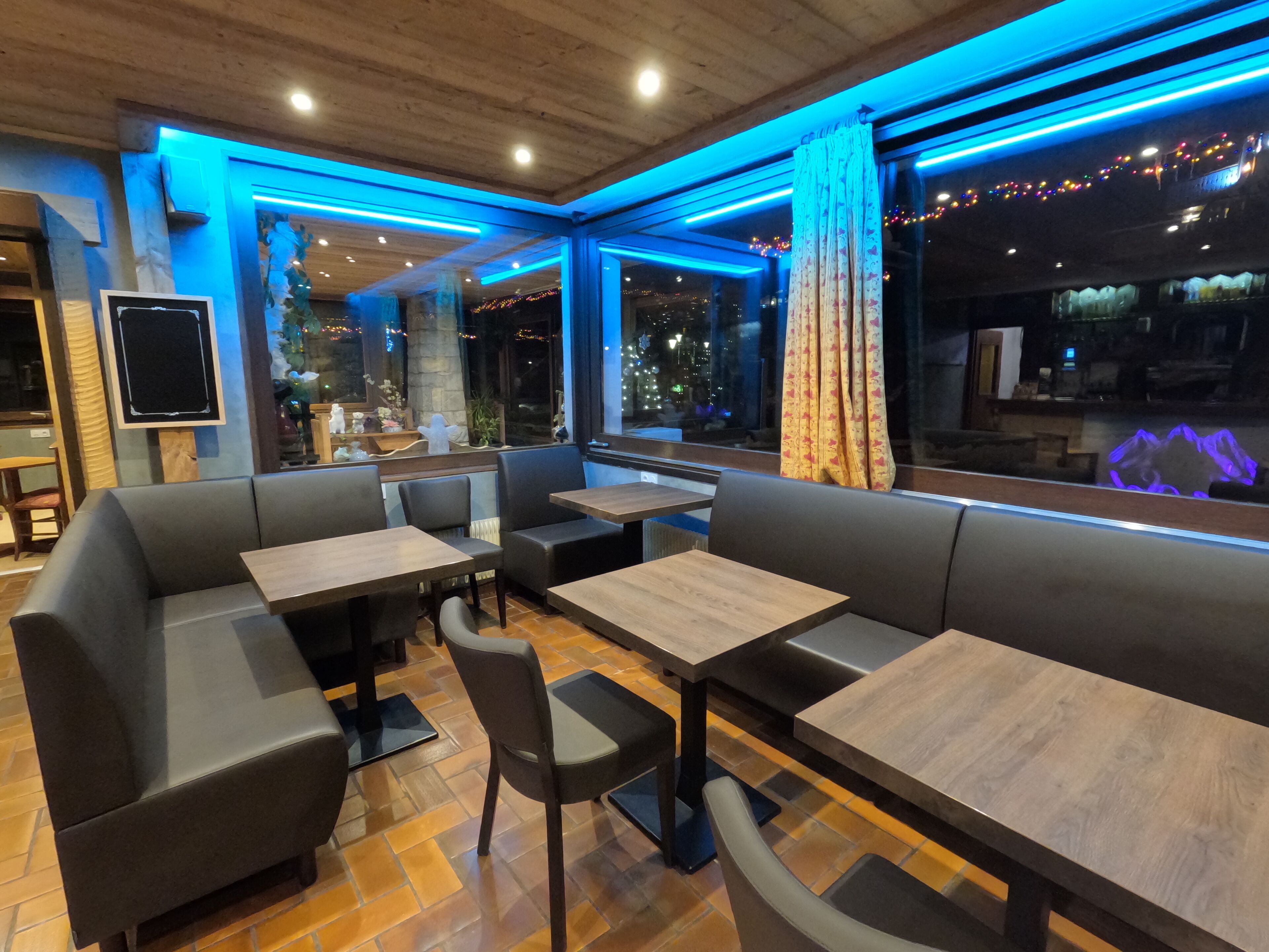 A restaurant interior with a modern design, featuring a mix of seating options including booths and tables, wooden flooring, and a view of the city at night.