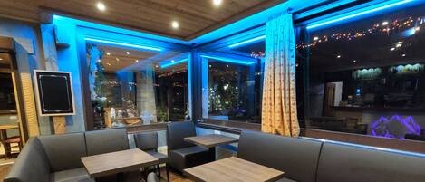 A restaurant interior with a modern design, featuring a mix of seating options including booths and tables, wooden flooring, and a view of the city at night.