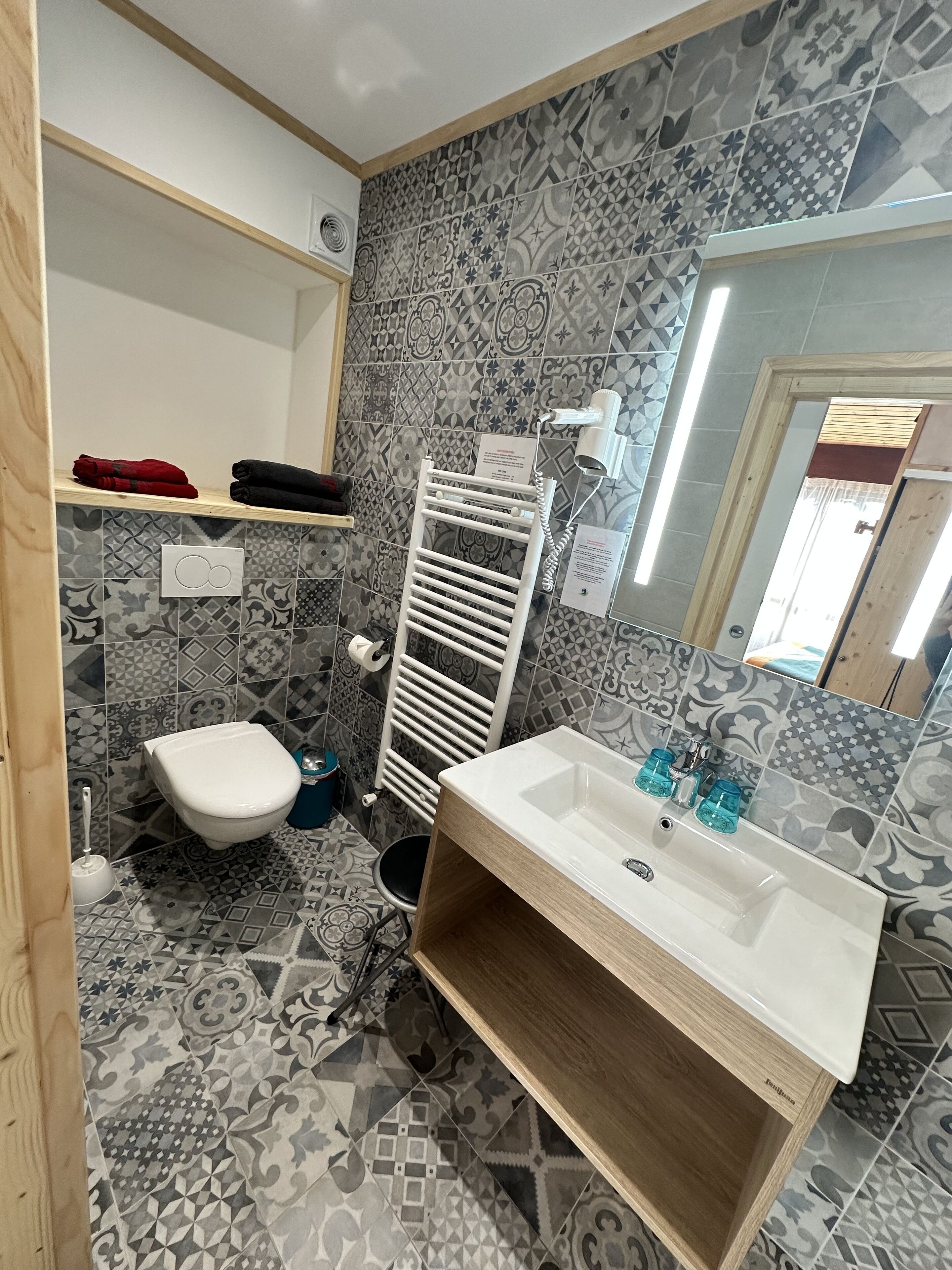 A bathroom with patterned tiles, a white toilet, a sink with a wooden vanity, and a towel rack.