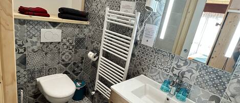 A bathroom with patterned tiles, a white toilet, a sink with a wooden vanity, and a towel rack.