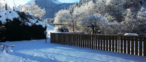 A snowy landscape with a wooden fence, trees, and a mountain in the background.