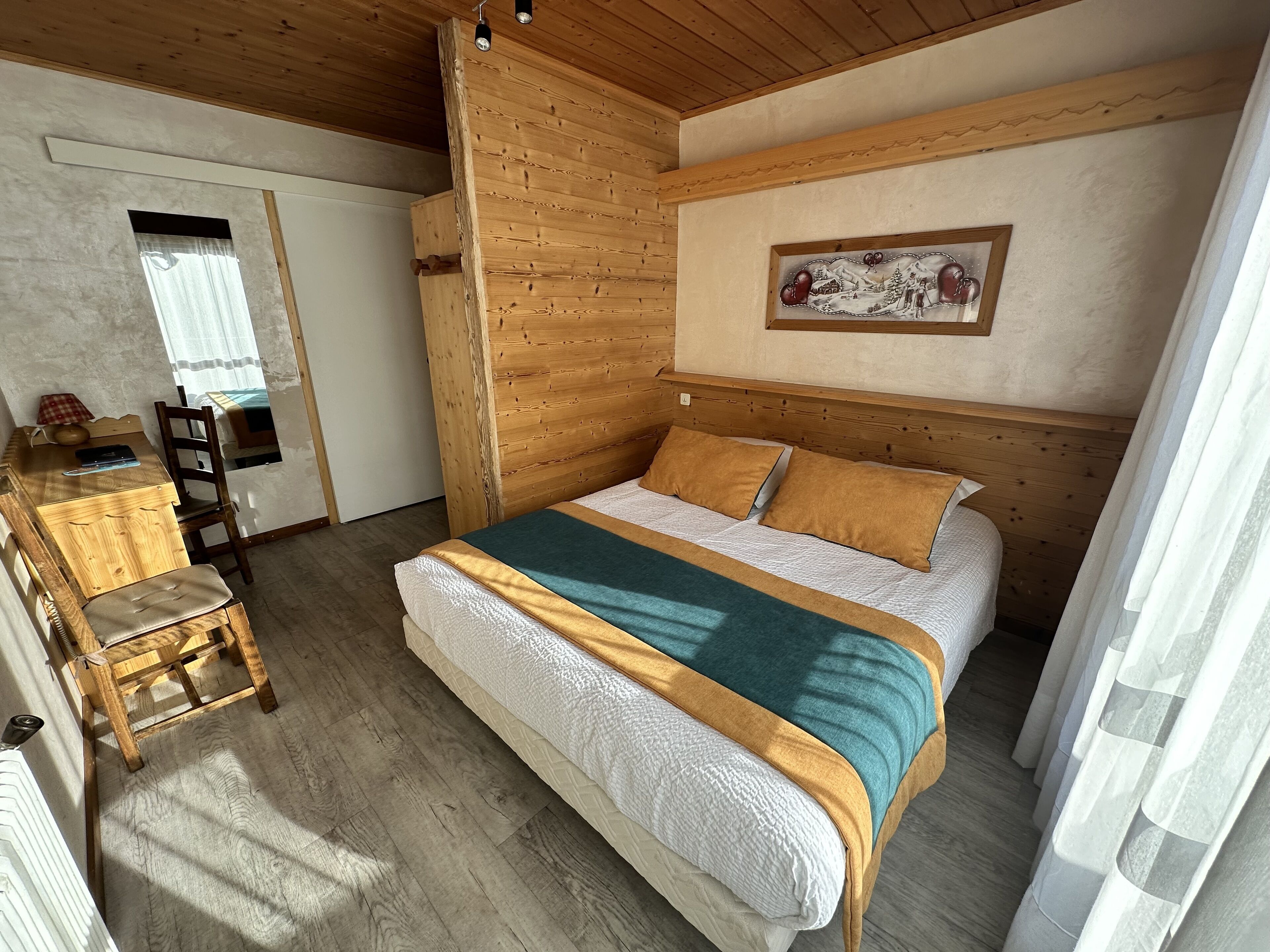 A bedroom with a wooden headboard, a bed with two pillows, a bedside table with a lamp, and a chair.