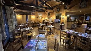 A cozy restaurant with wooden interiors, tables set for dining, and a bar area. - Le Soly Hotel (Morzine)