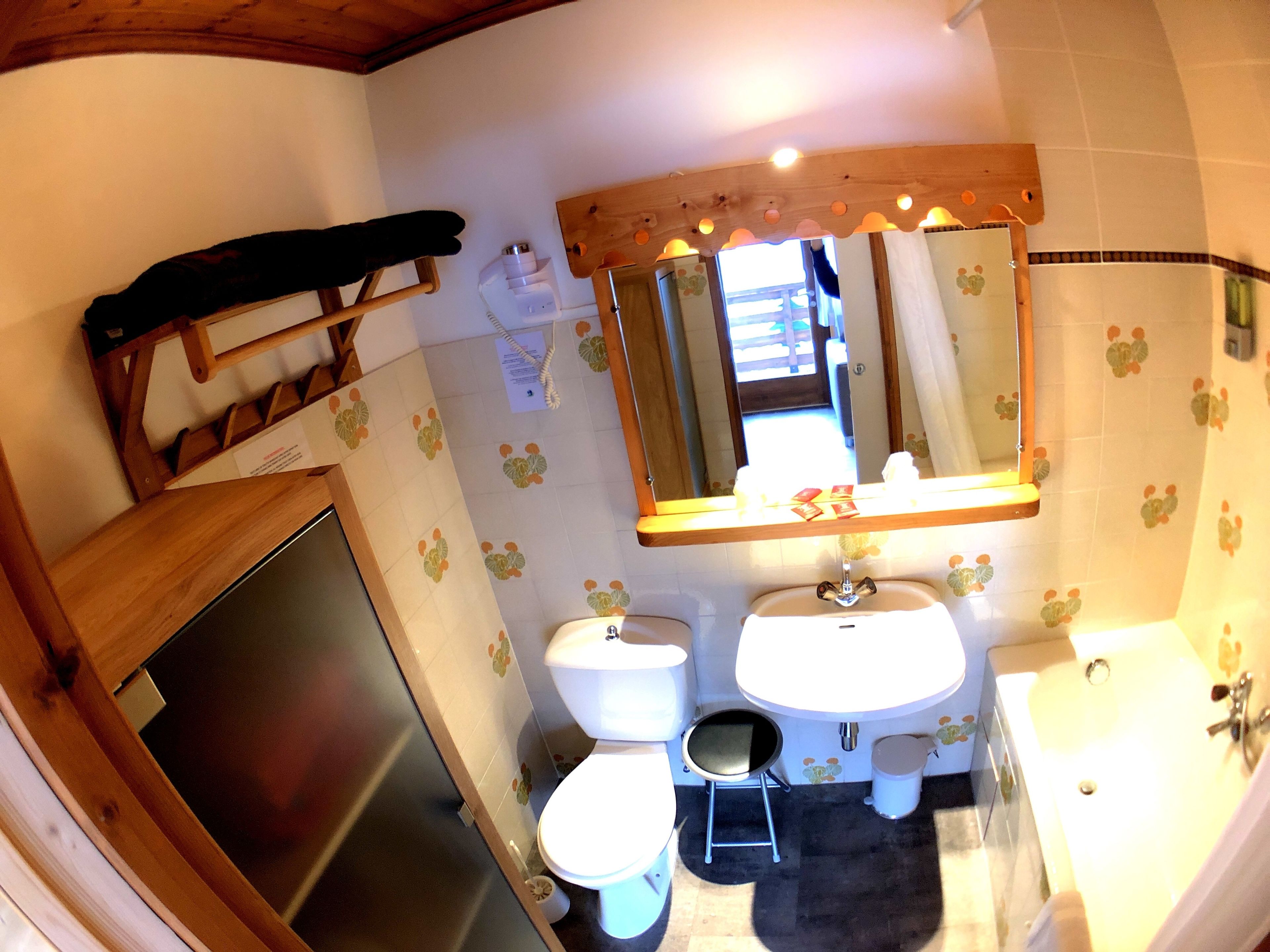 A bathroom with a wooden shelf, two sinks, a toilet, and a mirror.