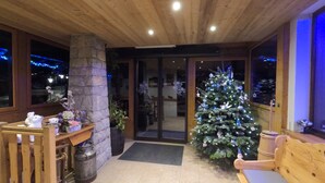 A cozy interior with a wooden ceiling, a stone pillar, a Christmas tree, and a bench. - Le Soly Hotel (Morzine)