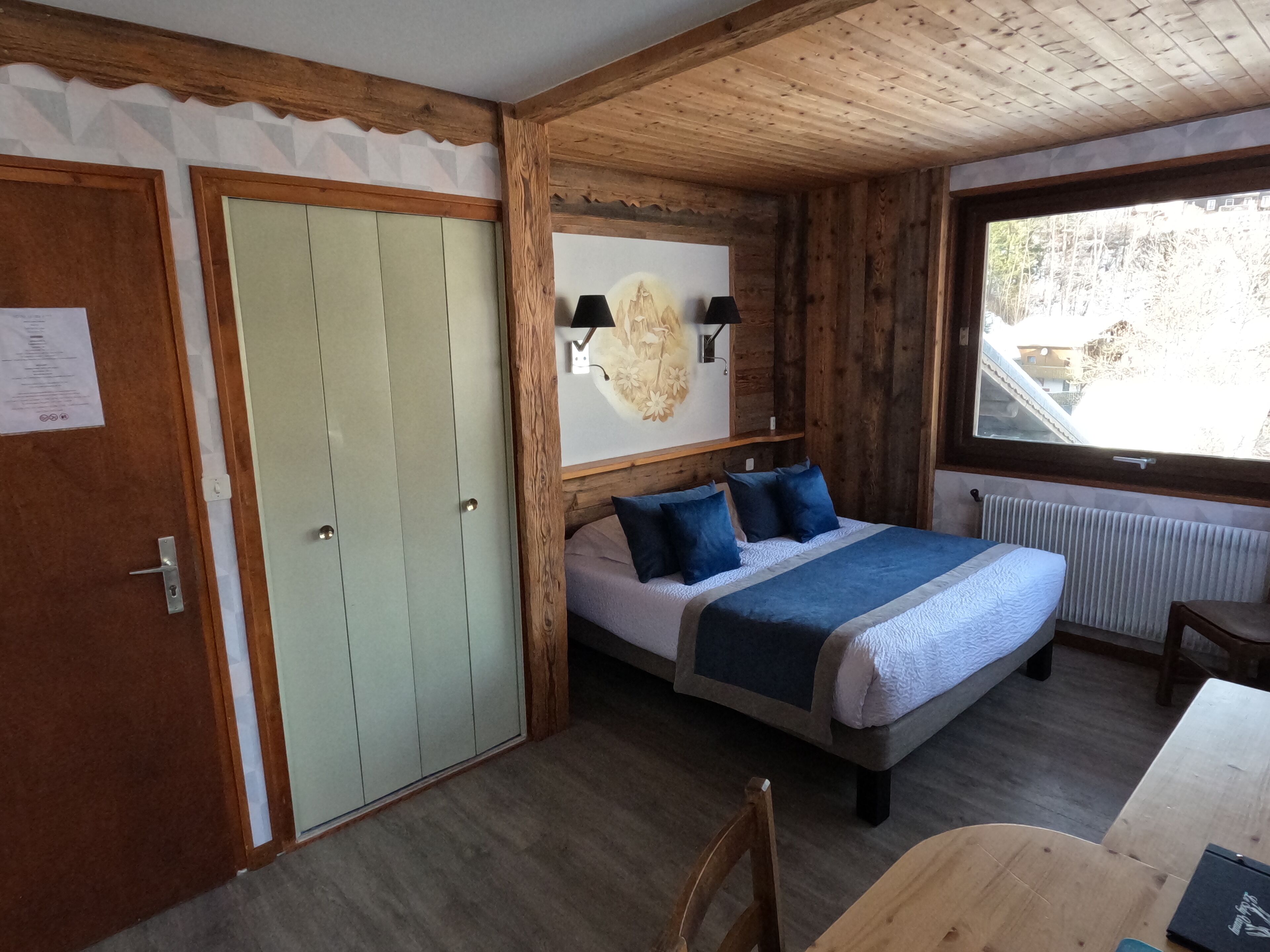 A wooden-paneled room with a bed, a table, and a window.