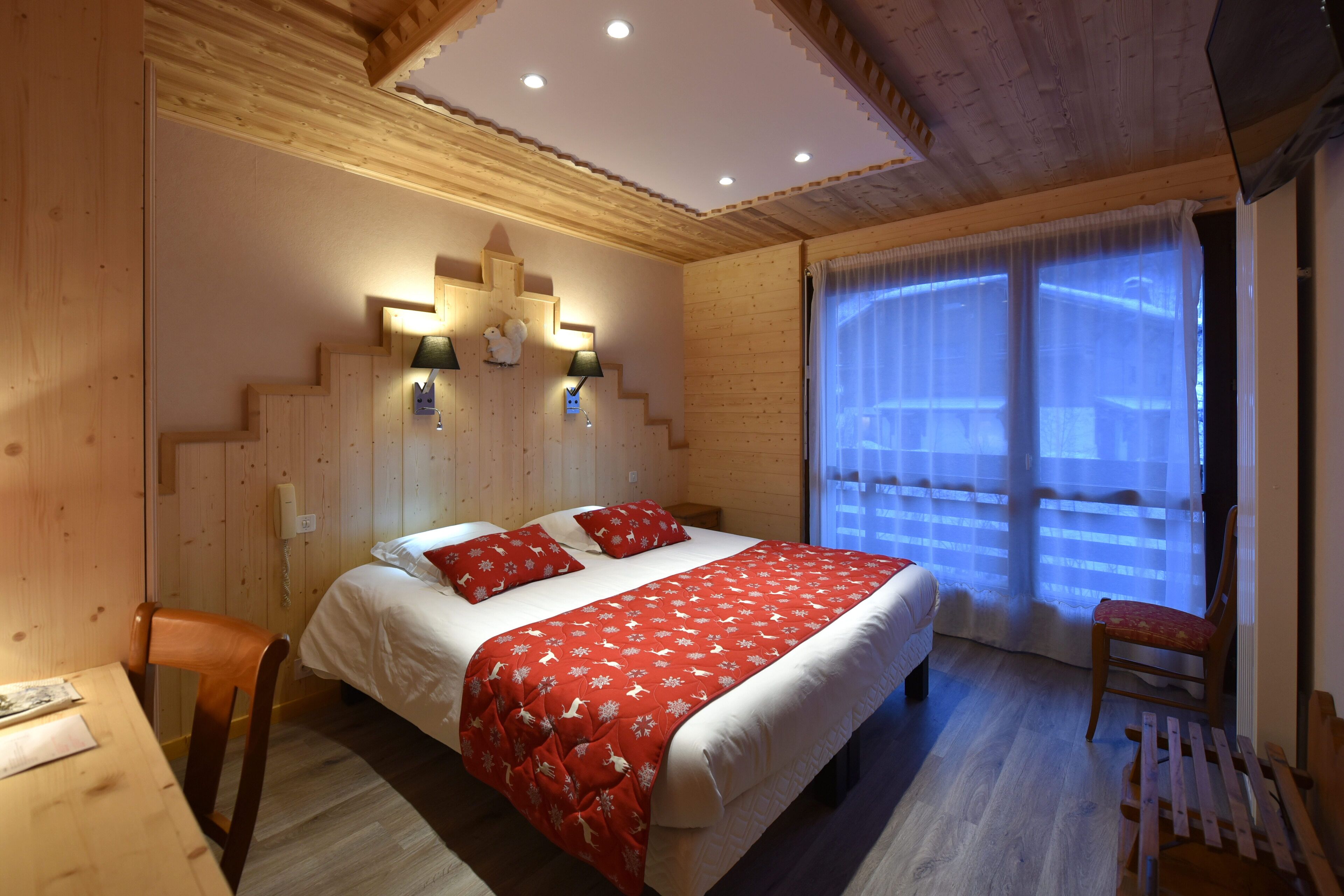 Une chambre à coucher aux murs lambrissés, avec un lit, des lampes de chevet et une fenêtre ornée de rideaux légers.