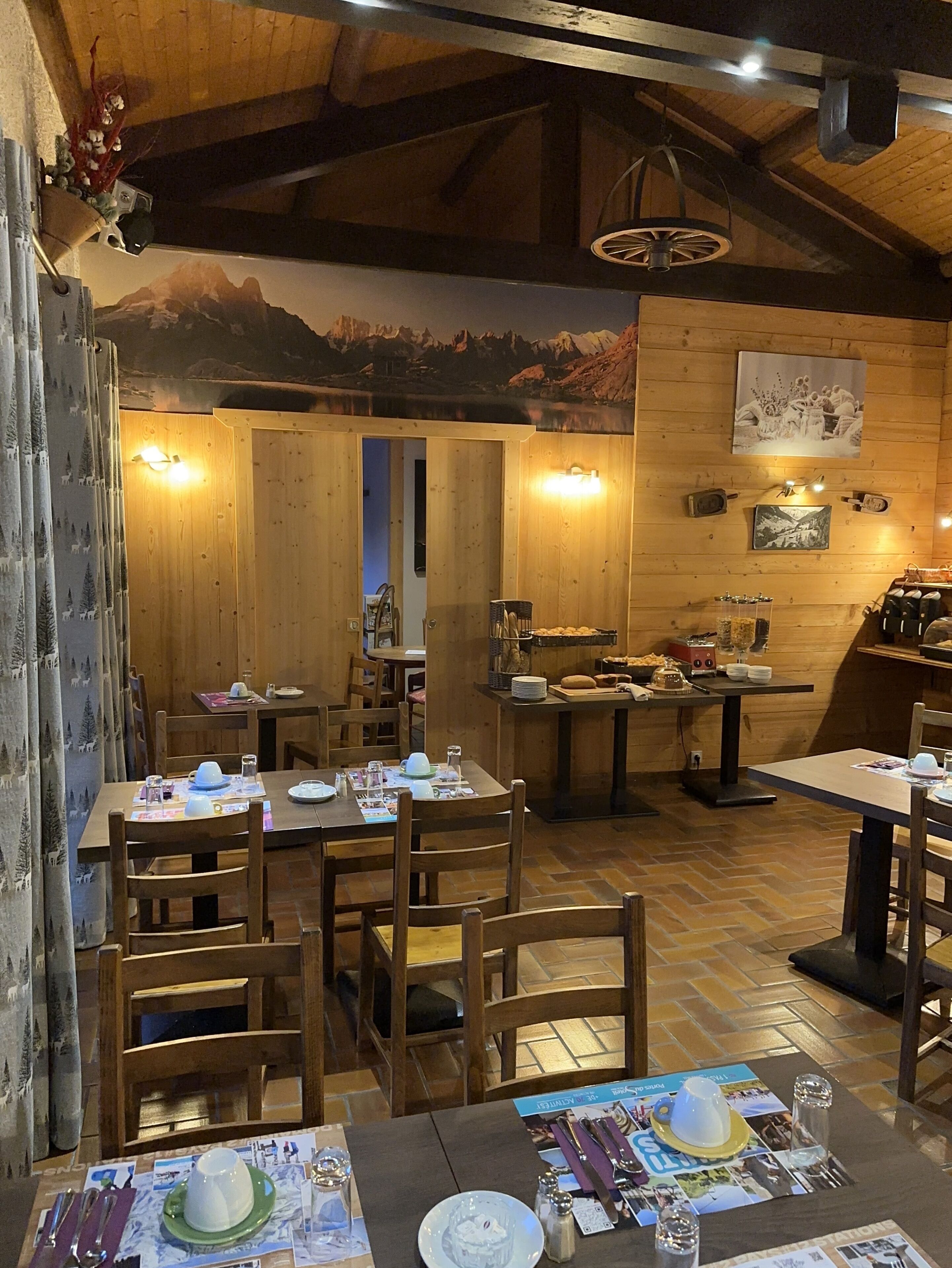A cozy restaurant with wooden interiors, wooden tables, and chairs, and a mural of a mountain landscape on the wall.