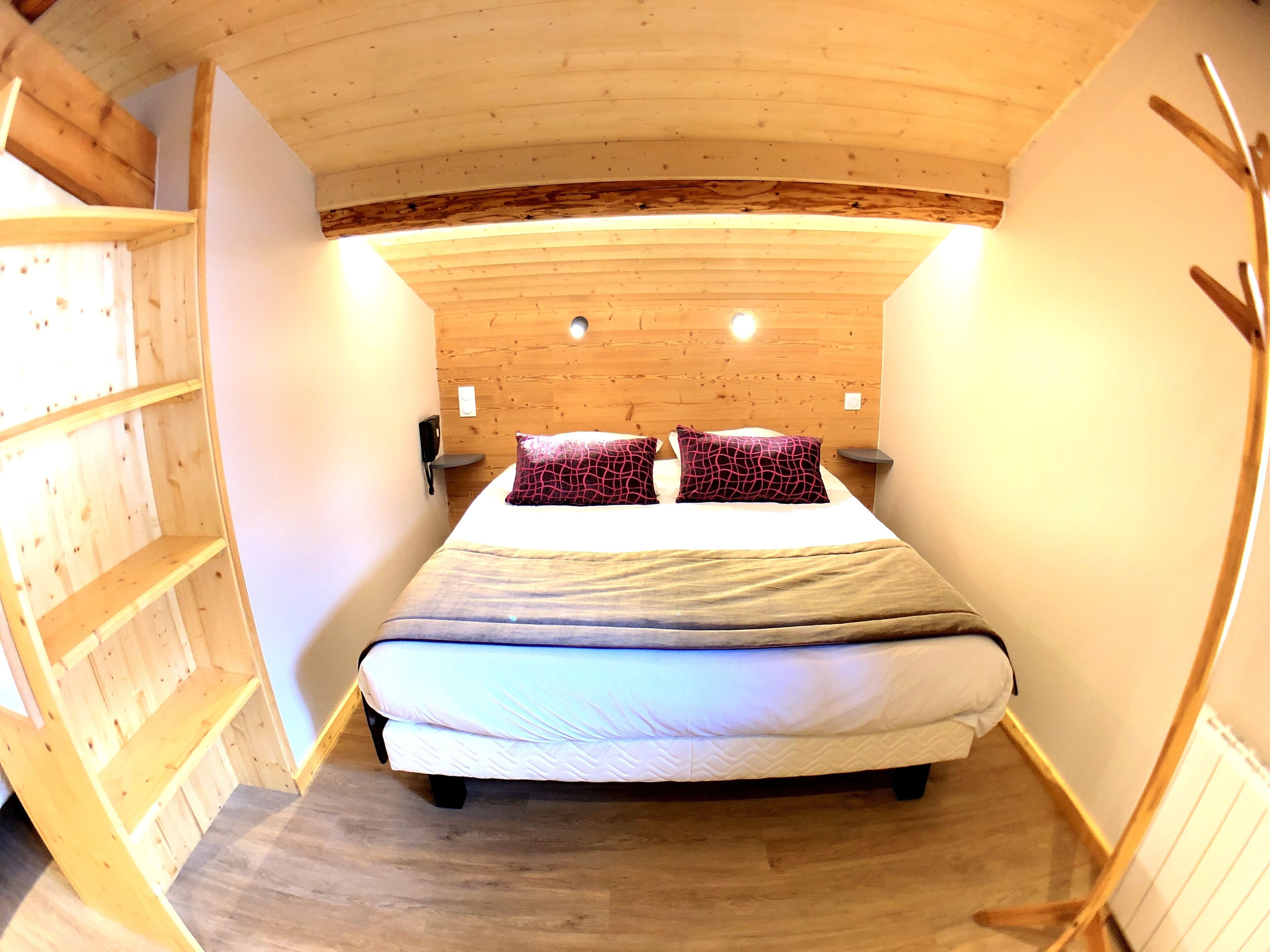 A cozy room with a wooden sloped ceiling, a bed with two patterned pillows, a bedside table, and a wall-mounted phone.
