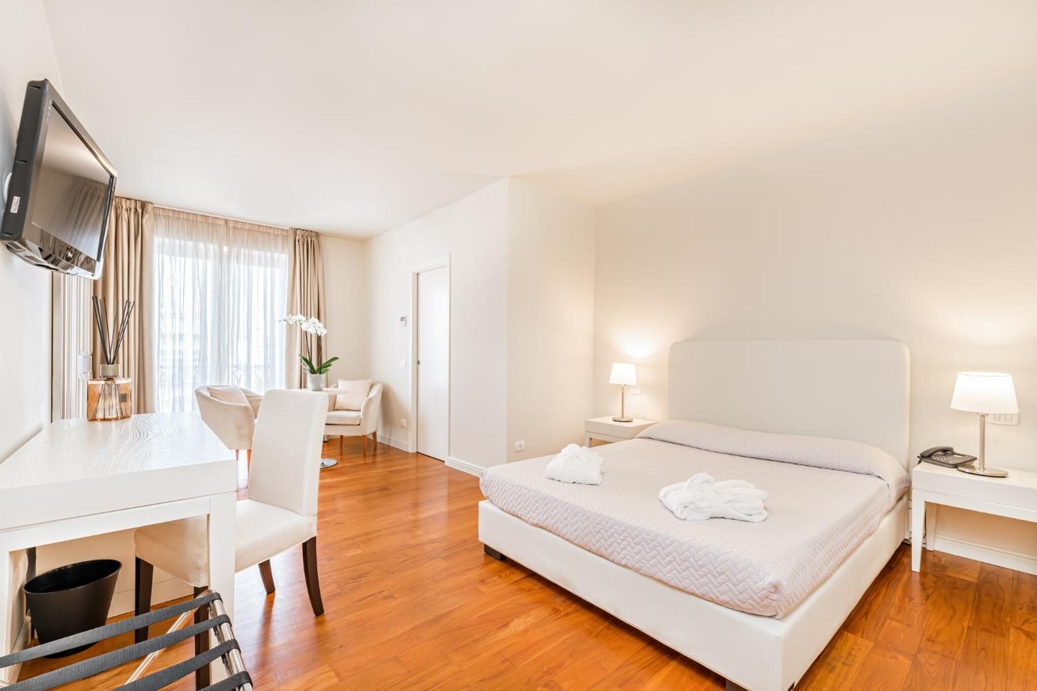 Ein Hotelzimmer mit Bett, Nachttisch, Fernseher und Schreibtisch mit Stühlen.