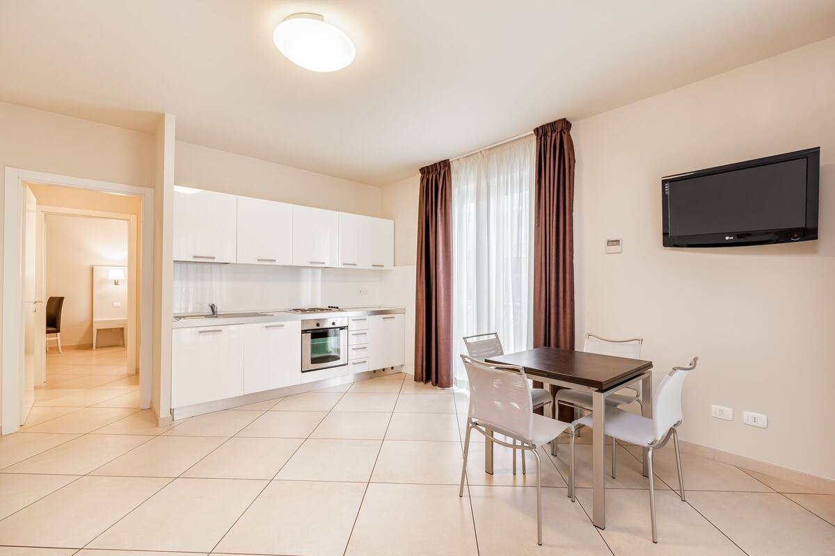 A modern kitchen with white cabinets, a built-in oven, and a dining area with a table and chairs.